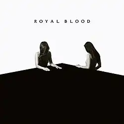 Two topless women sat beside a table against a white background. The band name is written above in the centre.
