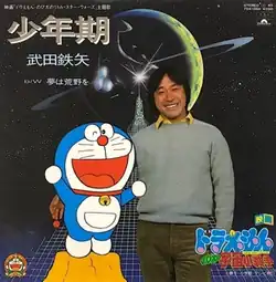 Tetsuya Takeda holding Doraemon on the album. It has "映画「ドラえもん　のび太のリトル・スター・ウォーズ」主題歌 少年期 武田鉄矢 b/w 夢は荒野を" at upper left, "STEREO 45, 7DX 1360 ¥700, Polydor" at upper right, and "ドラえもん　のび太の宇宙小戦争" at lower right