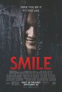The zipper of a partially open bodybag reveals the face of a woman with a rictus grin.
