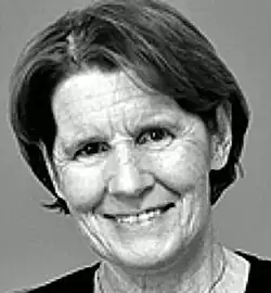 Black and white studio portrait of a smiling woman with little or no makeup, and short, straight, slightly greying hair.