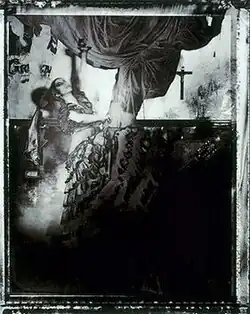 Blurred sepia-toned scene of a woman in a ruffled dress in mid-motion under draped fabric with a crucifix and guitar in the background