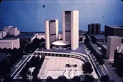 Two curved towers surrounding a circular small building with an open public space in front