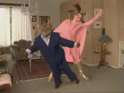 Björk in a pink dress dances around a human-sized cat in a suit.