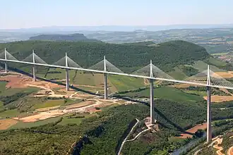 A large bridge, consisting of multiple tall sections, passing over a wide valley
