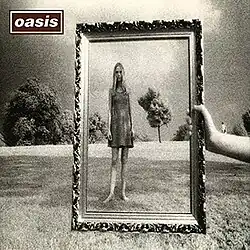 Wonderwall single cover art. A black and white photo with a hand holding a hollow picture frame, with a female figure inside it standing on a grassy hill. Trees are on the crest of the hill behind.