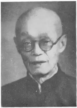 Black and white photo of an old bald man wearing thick rimmed glasses